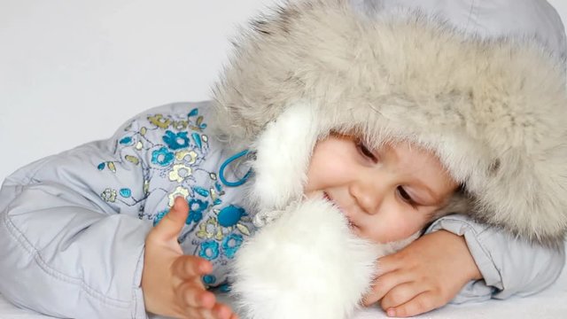 A funny child dressed in warm fur clothes and looking at the camera. Close-up portrait. The concept of winter, frost and snow, cold weather, cool temperature and Christmas.