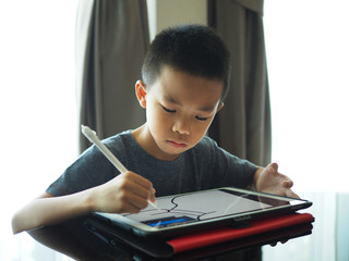 Asian boy doing digital drawing on tablet with high concentration.
