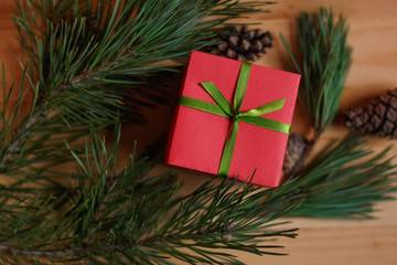 Fototapeta na wymiar Christmas still life: red box (gift), tied with green ribbon, among the spruce twigs and cones on wooden table