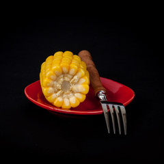 yellow fresh corn with fork on black background
