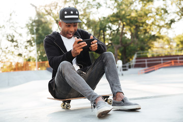 Young african man with a skateboard using smartphone
