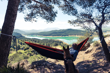 Wanderlust man and dog relaxing at hammock in mountains