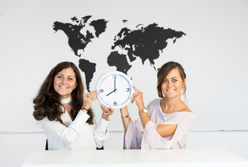 Two young girls twins with clock on the background of the world map