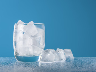 Empty glass with ice cube on blue background