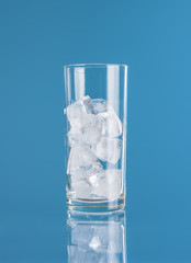 Empty glass with ice cube on blue background