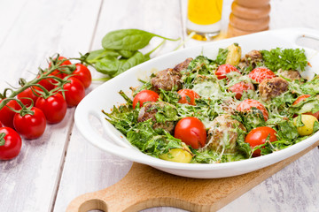 Meatballs and spinach oven dish with cherry tomatoes, potatoes and herbal cheese and cream sauce. One pot meal on White wood background.