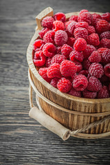 Tasty raspberries in bucket on vintage wooden board