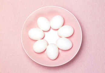 Top view of seven white egg on the pink plate and pink background