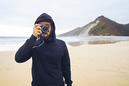 Hooded man taking a photo on the beach