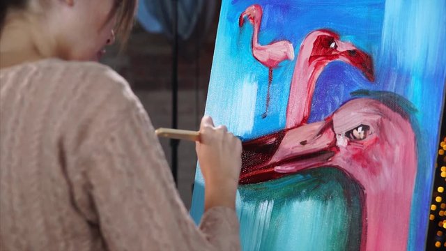 professional painter paints a painting with pink flamingos, animals are on a blue background, the woman is holding a brush