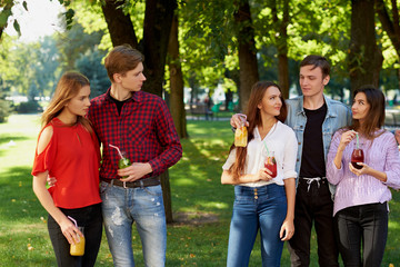 Jealousy and envy in friends relationship. Cheerful young people with detox cocktail having outdoor summer party