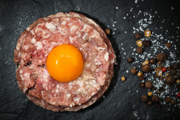 meat cutlet raw (minced) with raw egg, a mixture of peppers, peas and salt on a slate plate - tartar