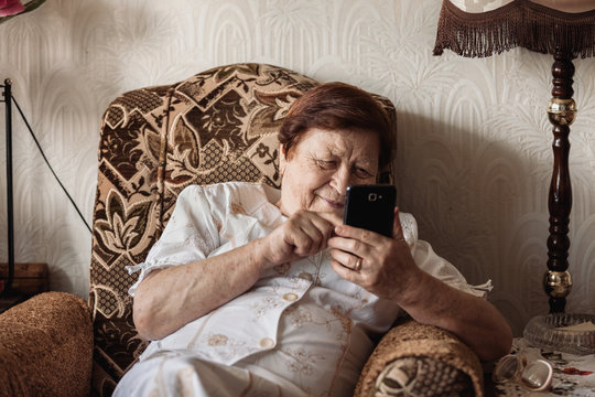 Old woman using smartphone (tablet) sitting in chair smiling