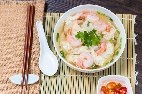 Shrimp wonton noodle soup with braised pork in soup on wooden table - Asian food style.