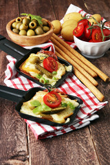 Delicious traditional Swiss melted raclette cheese on diced boiled or baked potato served in individual skillets with salami..