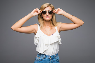 Young attractive lady in jeans and sunglasses posing in studio on grey background not isolated, blond girl hipster summer outfit concept, photo with place for text