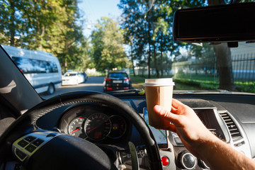 The driver is drinking coffee behind the wheel closeup. Transportation, drinks, people and vehicle concept - close up of man drinking coffee while driving car