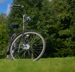 Fototapeta na wymiar black bike parked on the grass in a park with trees in the background