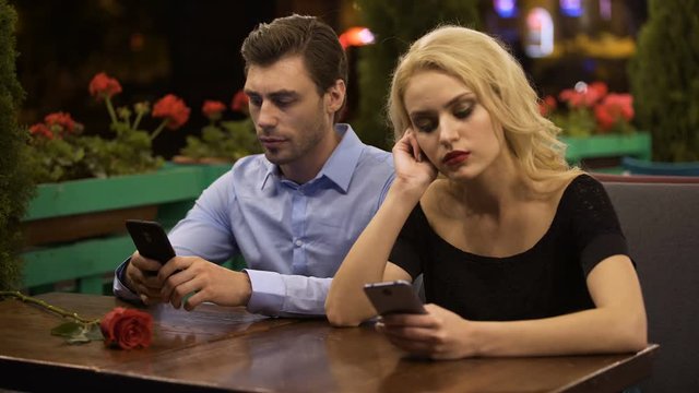 Two young people boring on date, using smartphones, problems in relationship