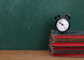 Small clock on books on desk, chalkboard background