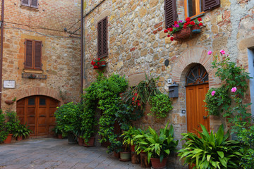 Fototapeta na wymiar Beautiful narrow street with sunlight and flowers in the small magical and old village of Pienza, Val D'Orcia Tuscany, Italy.