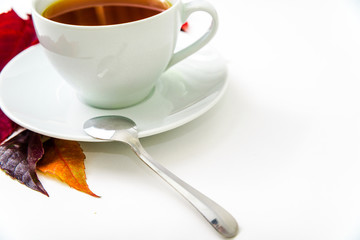 Cup of tea. Side view of a cup of tea with saucer on which lies a teaspoon. White background with red autumn leaves. Tea is best for cold autumn evenings and for depression.