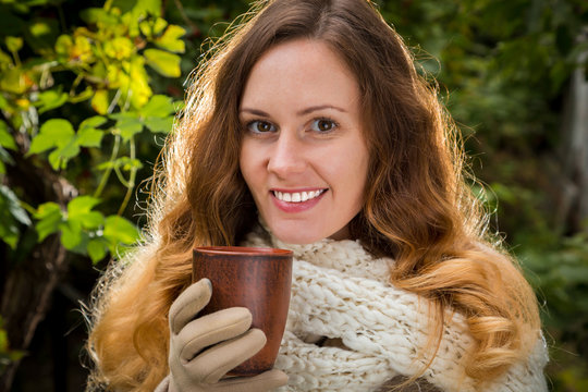 girl in warm clothes on autumn park holding a cup with hot bever