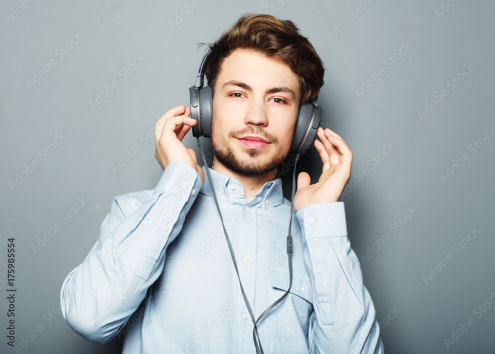 Poster  Happy young stylish man  adjusting his headphones ad smiling wh