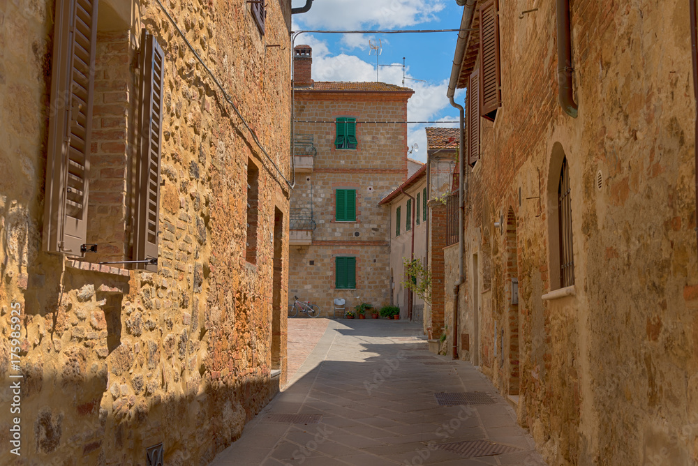 Wall mural Beautiful narrow street with sunlight and flowers in the small magical and old village of Pienza, Val D'Orcia Tuscany, Italy.