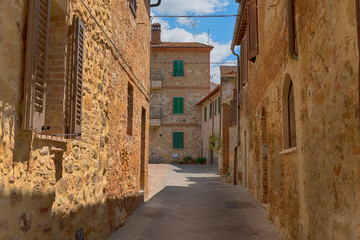 Beautiful narrow street with sunlight and flowers in the small magical and old village of Pienza, Val D'Orcia Tuscany, Italy.