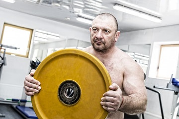 Naklejka na ściany i meble The adult brutal man is engaged in power bodybuilding in the gym