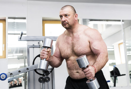 The adult brutal man is engaged in power bodybuilding in the gym