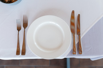 Empty white plate on a white tablecloth with knife and fork.  