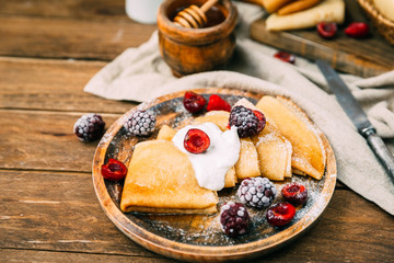pancakes with berries, jam and honey on wooden table