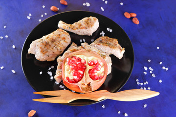 Steaks with grill on a black plate with a wooden fork, large salt, spices, pomegranate and peanuts on a dark blue background in retro style
