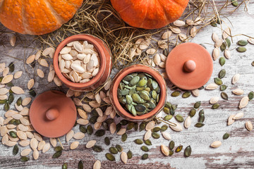 Colorful pumpkins and seeds in two ceramic jars on white rustic table with straw in studio