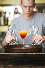 Young bartender making a colorful cocktail, pouring alcohol in a cocktail glass