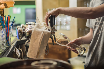 Pouring fresh beer. Close-up of young bartender pouring beer while standing at the bar counter
