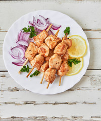 Grilled chicken skewers with pickled red onion and lemon on a light background. Delicious summer lunch, top view