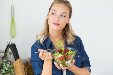 Beautiful young woman eating salad at home.