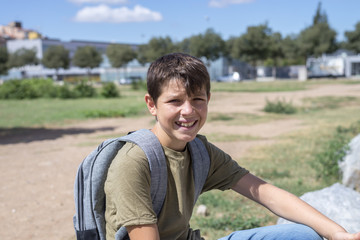 Cheerful child carrying his backpack sitting in front of the sc