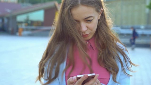 Young attractive blonde asian looks into the phone on the street. pleasant friendly face lifting. the dancer chooses the music on the phone. 4k