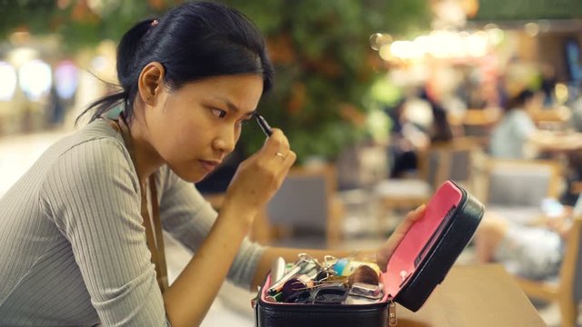 Asian Woman in mall applying mascara makeup on eyebrows. Toned video 4k UHD (3840x2160)
