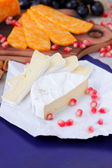 Camembert cheese, marbled cheese, different cheeses, dark blue grapes, red pomegranate, green grapes, peanuts and walnuts on a wooden board with an empty place for writing