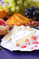 Camembert cheese, marbled cheese, different cheeses, dark blue grapes, red pomegranate, green grapes, peanuts and walnuts on a wooden board with an empty place for writing