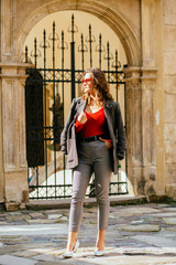 Vertical full height photo fashionable woman in high heel shoes, casual jacket and pants in a cage and red shirt posing over old city building background.Weekend, travel and leisure concept.