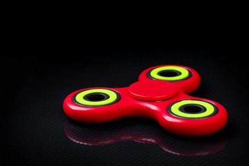 Close-up shot of red-green fidget finger spinner on black gloss background.