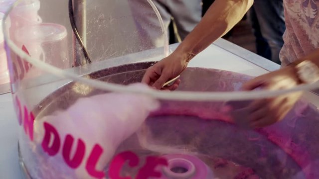 Close up of man or staff at amusement park or county fair carnival preparing sugar cotton candy, in awesome pink color. guilty pleasure high calory snack, childhood memories of attraction parks