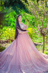 Fototapeta premium Beautiful girl in pink long dress, standing near blooming cherry, in park.