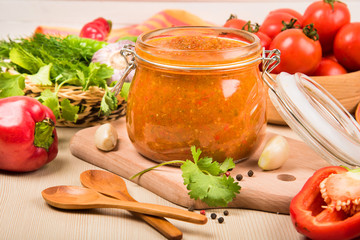 Tomato sauce (ketchup, adzhika) and vegetables on a beige table. Home preservation.